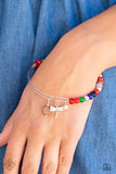 A charismatic collection of multicolored stone beads is threaded along a skinny silver wire, as it curls into a dainty bangle. Silver beads are mixed along the colorful display, adding hints of metallic sheen, as a wooden disc, a singular white stone bead, and a silver dragonfly charm slide and sway in a whimsical finish.  Sold as one individual bracelet.