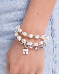 Alternating with silver beads, two strands of elongated pearls join around the wrist, creating timeless layers. A third chain layer with a key lock featuring the stamped word "love" and a heart finishes off the design with a romantic touch. Features an adjustable clasp closure.  Sold as one individual bracelet.