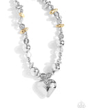 Infused along an invisible string, a collection of silver beads in varying sizes, chiseled gold pebbles, and transparent gray beads loop around the neckline for a glistening display of color. An oversized silver heart pendant swings from the center of the display for a light-hearted finish. Features an adjustable clasp closure.  Sold as one individual necklace. Includes one pair of matching earrings. 