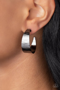 Etched in glistening linear patterns, a flat gunmetal ribbon widens at the center as it curls into a curvaceous hoop. Earring attaches to a standard post fitting. Hoop measures approximately 1 1/2" in diameter.