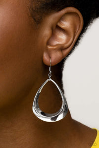 A thick, asymmetrical silver teardrop frame glides from the ear, creating an unexpectedly refined statement. Earring attaches to a standard fishhook fitting.  Sold as one pair of earrings.