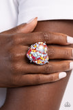 Encased within an exaggerated heart frame, dainty red and blue hearts with flecks of iridescence pattern into a kaleidoscope of color atop the finger on airy bands for a flirty finish. Features a stretchy band for a flexible fit. Due to its prismatic palette, color may vary.  Sold as one individual ring.