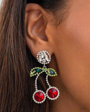 Embedded in glittery white rhinestones, various-shaped red and green rhinestones form two, vibrant cherries that swing from an exaggerated white gem post for a fantastic display of fruit. Earring attaches to a standard post fitting.  Sold as one pair of post earring